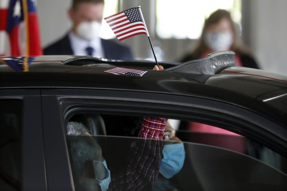 In this June 26, 2020 photo, a new U.S. citizen waves an American flag through the sunroof during a drive-thru naturalization service in a parking structure at the U.S. Citizenship and Immigration Services headquarters on Detroit's east side. The ceremony is a way to continue working as the federal courthouse is shut down due to Coronavirus. The U.S. has resumed swearing in new citizens but the oath ceremonies aren't the same because of COVID-19 and a budget crisis at the citizenship agency threatens to stall them again. (AP Photo/Carlos Osorio)