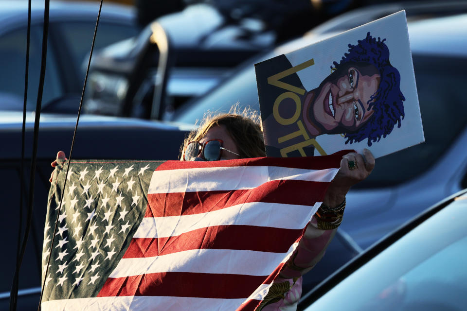 SAVANNAH, GEORGIA - JANUARY 03: A woman waves an American flag as she holds a painting of Stacey Abrams as she listens to Democratic Senate candidate Rev. Raphael Warnock speak during a drive-in rally at Garden City Stadium on January 03, 2021 in Savannah, Georgia. Vice President-elect Kamala Harris joined Warnock and fellow Democratic Senate candidate Jon Ossoff for a campaign event two days before the January 5th runoff election that has implications into which party controls the U.S. Senate. According to AJC, 3 million people have already casted their votes ahead of Tuesday's election.  (Photo by Michael M. Santiago/Getty Images)