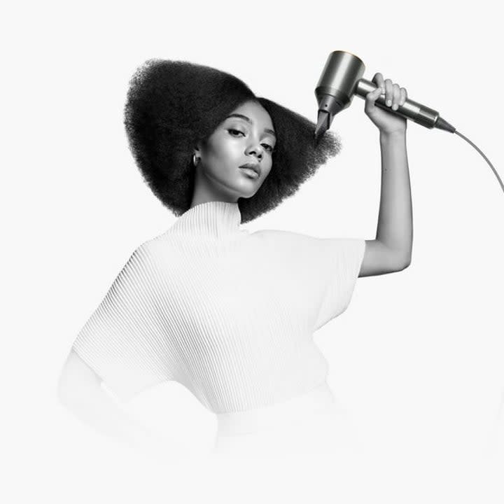 a woman styling her hair with a dyson hair dryer in black and white