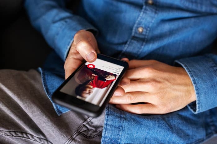 Close-up of a person using a dating app on their phone, wearing a denim shirt and grey pants