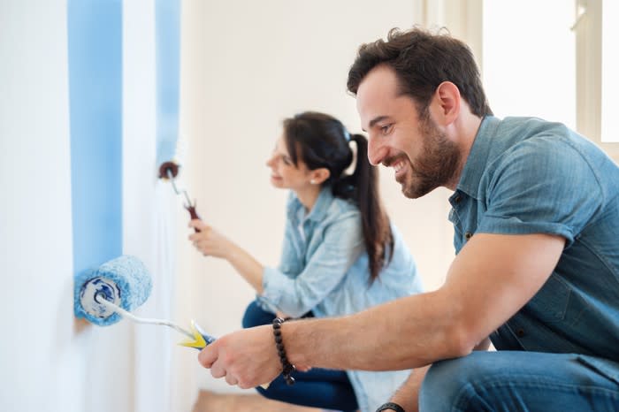 A man and woman paint the wall with rollers in a room.