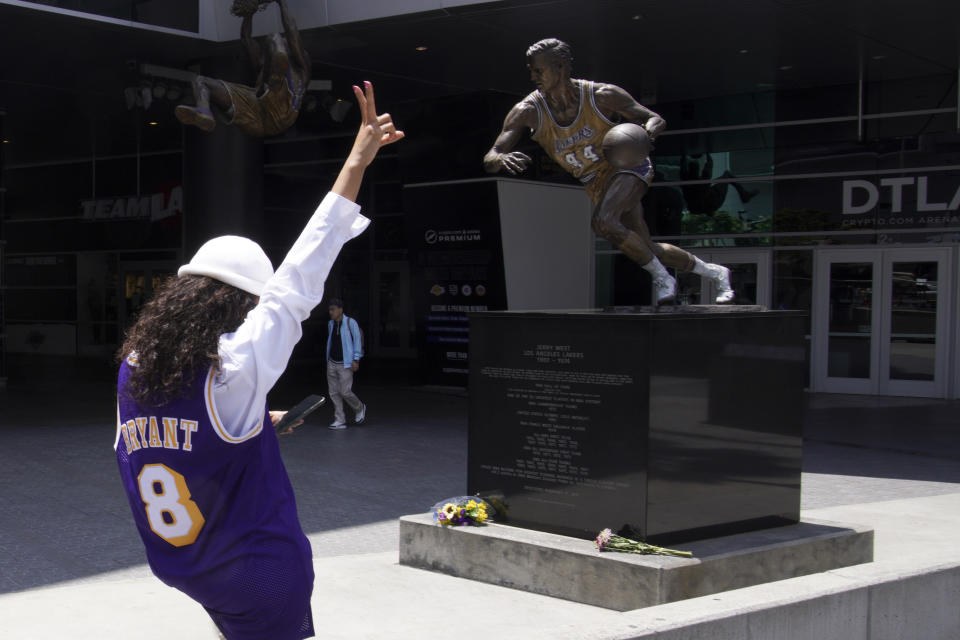 A fan gestures next to a statue of Jerry West outside of the Crypto.com Arena Wednesday, June 12, 2024, in Los Angeles. West, who was selected to the Basketball Hall of Fame three times in a storied career as a player and executive, and whose silhouette is considered to be the basis of the NBA logo, died Wednesday morning. He was 86. (AP Photo/Richard Vogel)