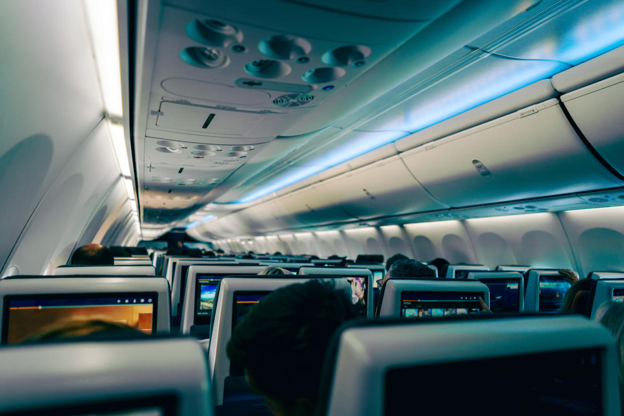 A rear view of seats on an airplane with lights and TVs turned on on the flight. (Photo via Getty Images)