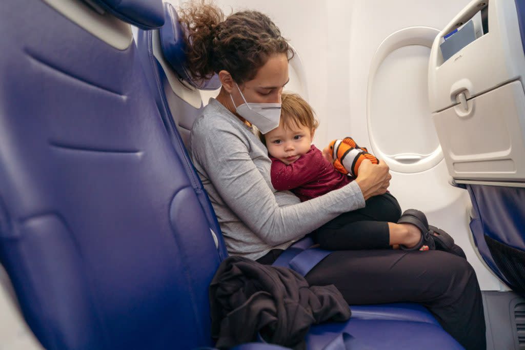 A mother wears a face mask while cuddling with her child on a plane. 