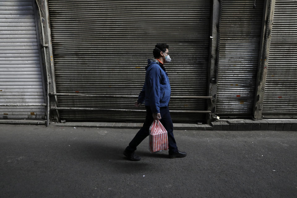 In this Tuesday, March 17, 2020, photo, a man wearing a face mask and gloves to help protect against the new coronavirus, walks in front of closed shops at the Tehran's Grand Bazaar, Iran. The new coronavirus ravaging Iran is cutting into celebrations marking the Persian New Year, known as Nowruz. (AP Photo/Vahid Salemi)