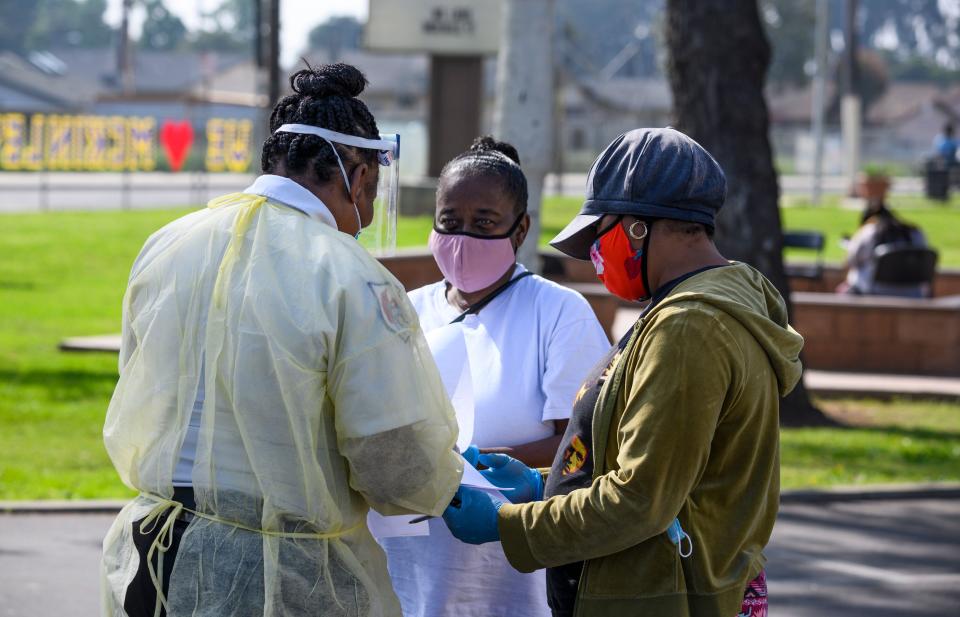 Local residents Burnetta Kinsey (C) and Zina Parker (R) fill out paperwork at a mobile COVID-19 testing station in a public school parking area in Compton, California, just south of Los Angeles, on April 28, 2020. - St. John's Well Child and Family Center is providing COVID-19 testing sites in African-American and Latino communities which have been neglected in terms of testing as compared to wealthier areas of Los Angeles County. (Photo by Robyn Beck / AFP) (Photo by ROBYN BECK/AFP via Getty Images)