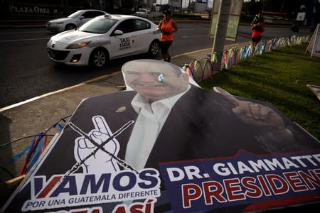 A woman runs in front of a campaign signs for Alejandro Giammattei, presidential candidate of "Vamos" political party, ahead of the second round run-off vote, in Guatemala City