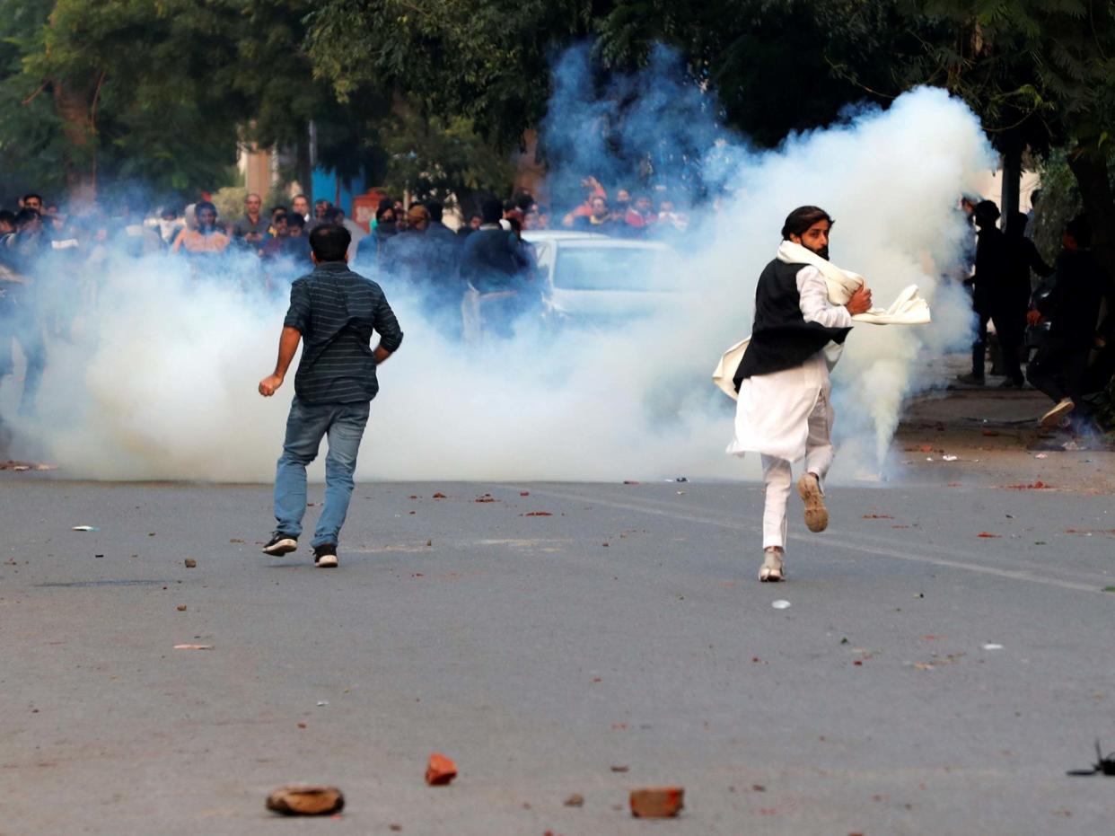 Demonstrators run for cover as smoke billows from a tear gas shell fired during a protest against a new citizenship law in New Delhi, India, 15 December, 2019: Reuters