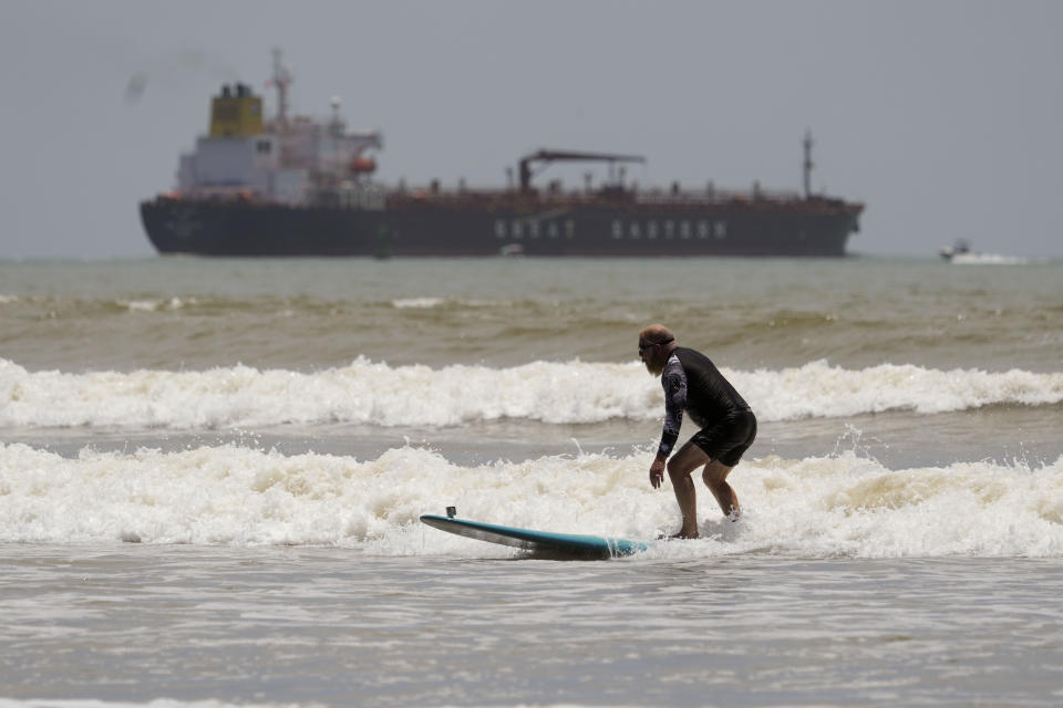 An oil tanker heads out to open water as a surfer takes advantage of waves ahead of Hurricane Beryl's arrival in Port Aransas, Texas, Saturday, July 6, 2024. (AP Photo/Eric Gay)