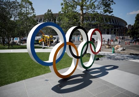 Construction workers and passersby are seen through Olympic rings in front of the construction site of the New National Stadium, in Tokyo