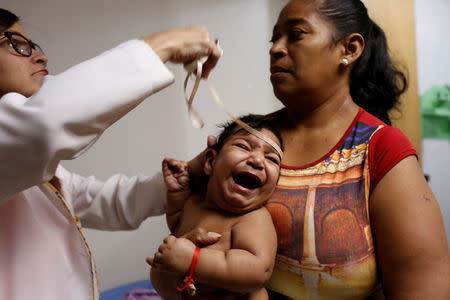 Iberis Vargas (R), holds her 7-month-old daughter, Geovelis Ramos, a neurological patient being treated with anticonvulsants, while an specialist examines her in a clinic in La Guaira, Venezuela February 4, 2017. REUTERS/Carlos Garcia Rawlins