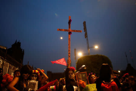 An activist with her face painted to look like the popular Mexican figure "Catrina" holds a cross as she takes part in a march against femicide during the Day of the Dead in Mexico City, Mexico, November 1, 2017. The words on the cross read: "No one more". REUTERS/Carlos Jasso