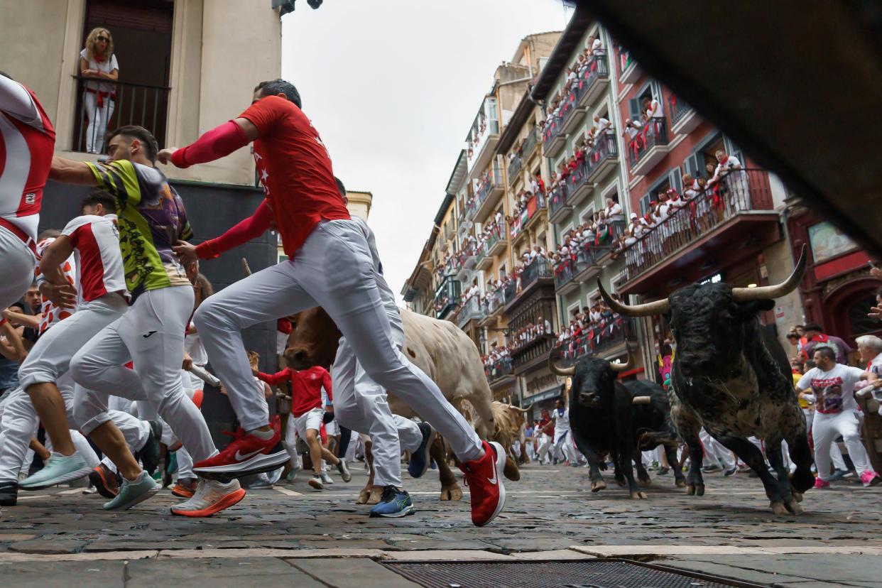 Participants run ahead of the bulls during a bull run as onlookers watch from the balconies above.