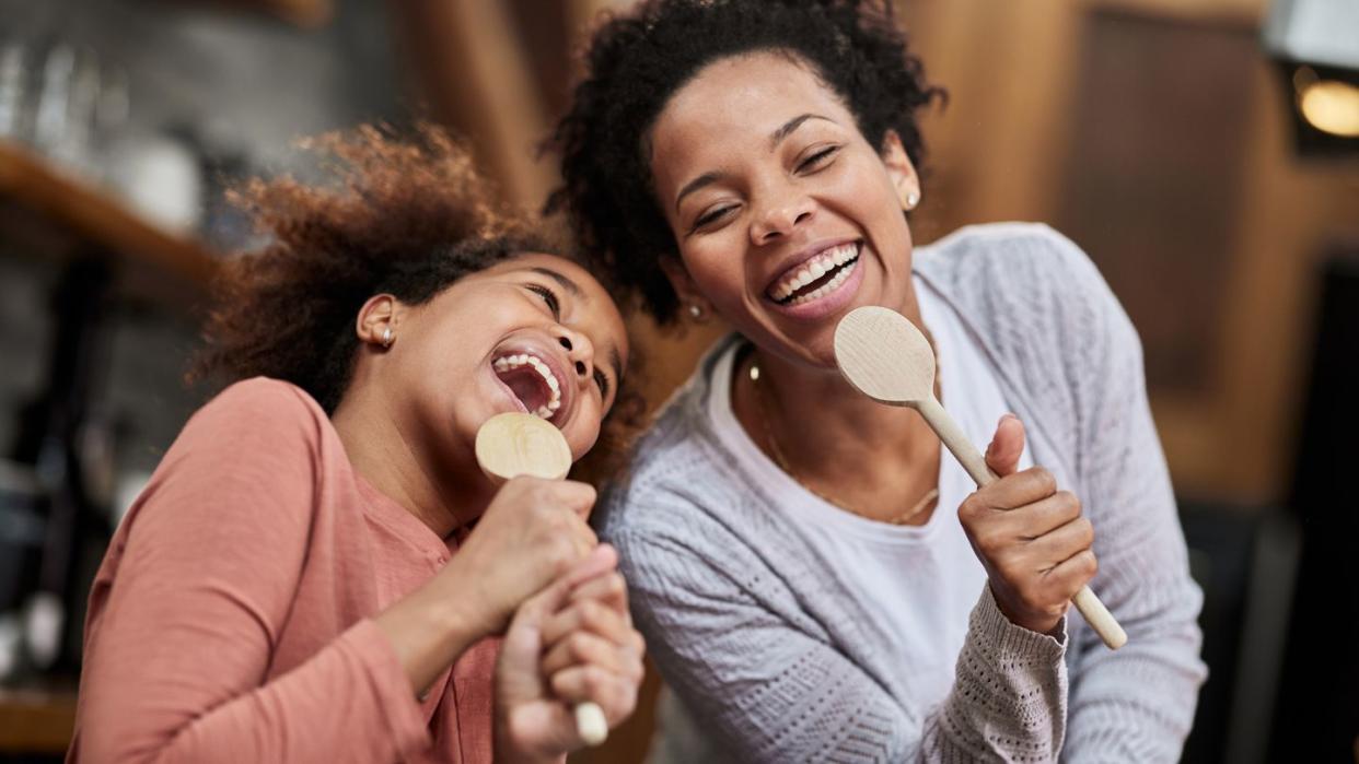 happy mother and daughter singing with wooden spoons at home