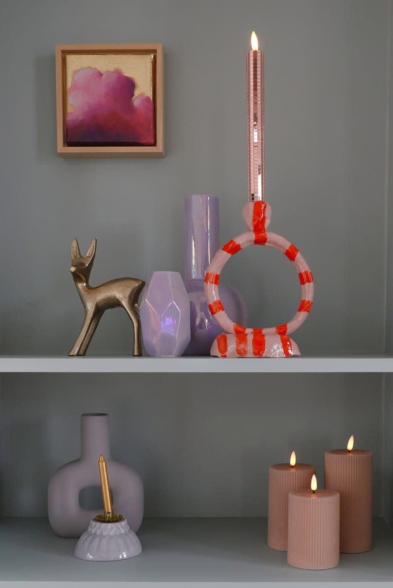 Pink candles and purple objects sit on gray shelf in houseboat.