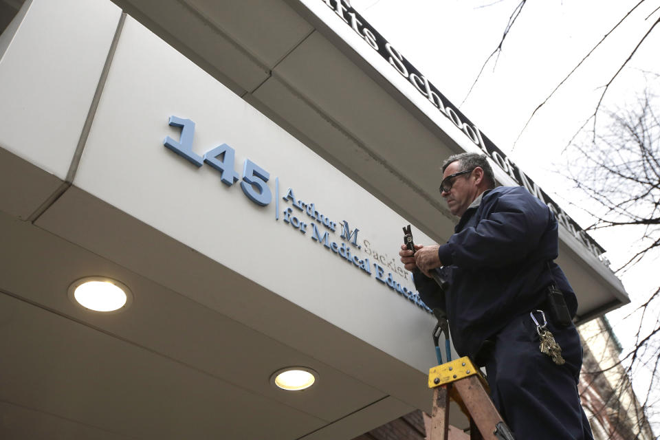 Worker Gabe Ryan removes a sign that includes the name Arthur M. Sackler at an entrance to Tufts School of Medicine, Thursday, Dec. 5, 2019, in Boston. Tufts University says it is stripping the Sackler name from its campus in recognition of the family's connection to the opioid crisis. (AP Photo/Steven Senne)