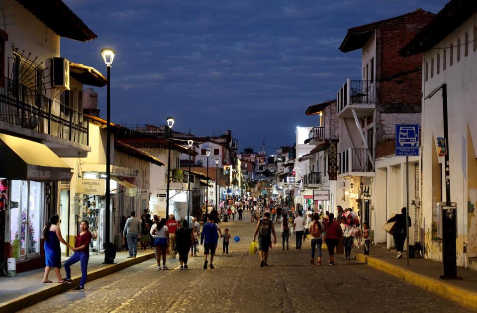 Pedestrians walking after dusk on a street flanked by Spanish colonial-style buildings