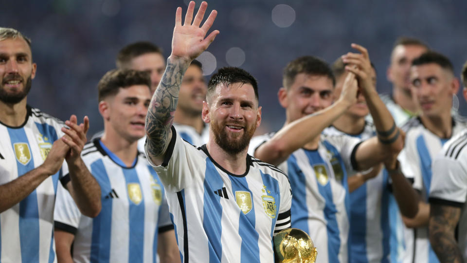 An image of Lionel Messi holding the World Cup while waving to fans, surrounded by his Argentina teammates