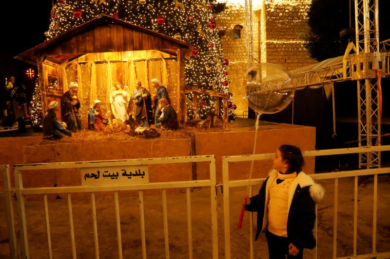 Girl looks at an artwork showing a nativity scene made of olive wood at Manger Square in Bethlehem in the Israeli-occupied West Bank
