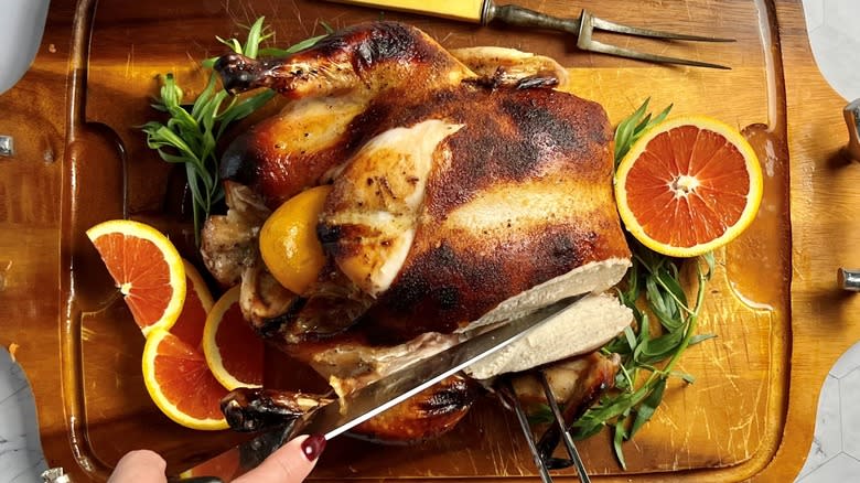 carving whole roasted chicken on wooden board