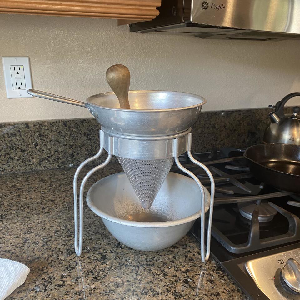 large metal masher set over a bowl with a wooden mallet for mushing fruit