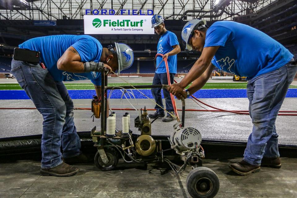 An installation crew sews together panels of FieldTurf Classic HD artificial turf at the Detroit Lions' Ford Field in Detroit, photographed on Thursday, May 9, 2019. The installation is expected to take four weeks and started on May 1st. 