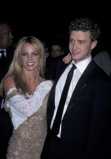 Britney Spears wearing a white and brown dress and Justin Timberlake wearing a suit are posing for photos