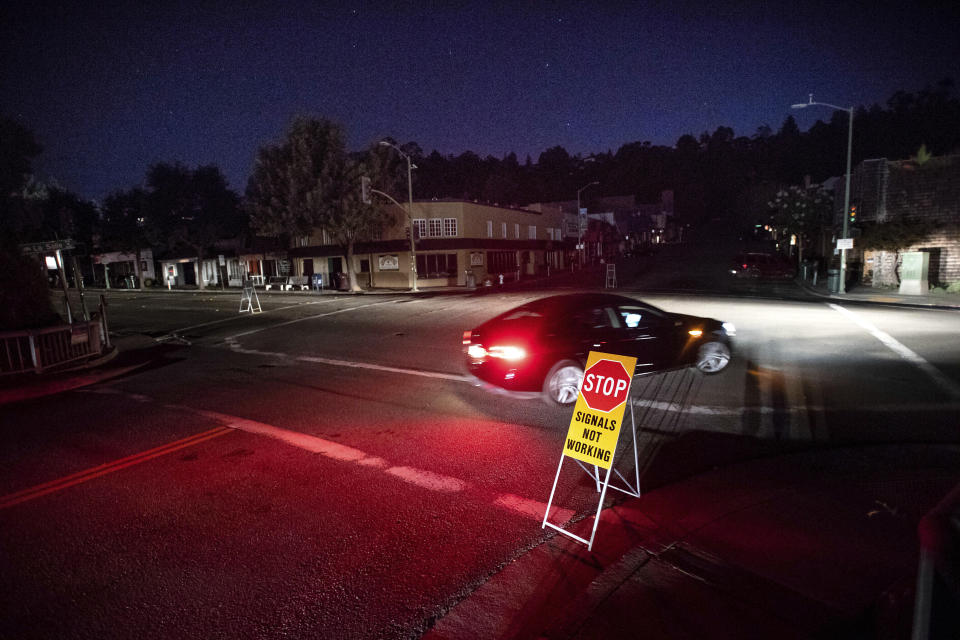 FILE - In this Oct. 10, 2019 file photo a car drives through a darkened Montclair Village as Pacific Gas & Electric power shutdowns continue in Oakland, Calif. Pacific Gas and Electric promised regulators Thursday, Aug. 13, 2020, that it has learned from its mishandling of deliberate blackouts and won't disrupt as many people's lives during the pandemic this year, when the utility expects to rely on outages to prevent its outdated grid from starting deadly fires. (AP Photo/Noah Berger, File)