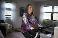 Catherine Busa rides an exercise bike as part of her recovery from COVID-19 at her home in New York, Wednesday, Jan. 13, 2021. The 54-year-old New York City school secretary didn’t have any underlying health problems when she caught the coronavirus in March and recovered at her Queens home. But some symptoms lingered. After eights months of suffering, she made her way to Jamaica Hospital Medical Center — to a clinic specifically for post-COVID-19 care. (AP Photo/Seth Wenig)