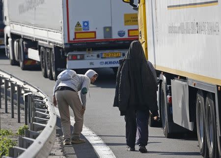 Migrants check the trailer of a truck during an attempt to make a clandestine crossing to England through the Channel tunnel as lorries wait on a road which leads to the Channel Tunnel terminal in Coquelles near Calais, northern France, July 1, 2015. REUTERS/Vincent Kessler