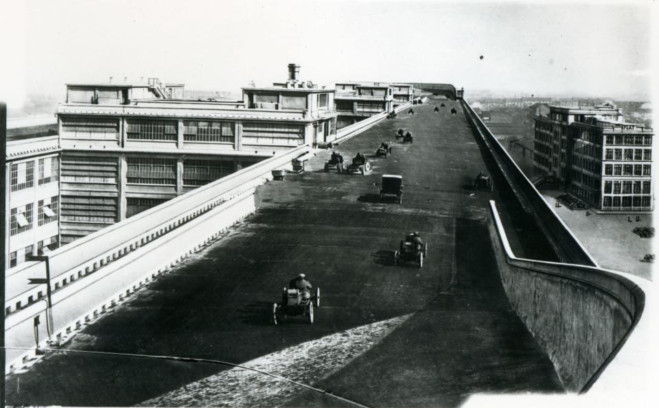 A test track on the roof of a building with very old-timey cars being driven on it