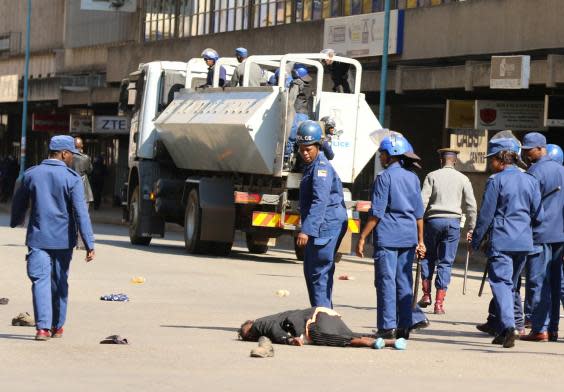 Police stand beside a woman injured during clashes after police banned planned protests over austerity and rising living costs called by the opposition Movement for Democratic Change (MDC) party in Harare, Zimbabwe (REUTERS)
