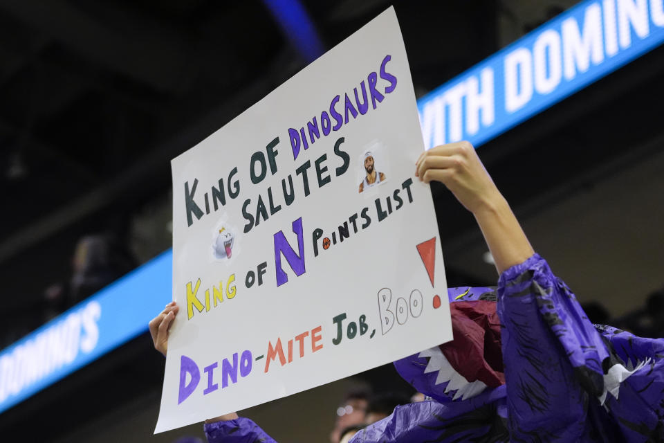 A fan in a dinosaur costume holds a sign after Northwestern guard Boo Buie became Northwestern's all-time leading scorer, during the first half of the team's NCAA college basketball game against Michigan, Thursday, Feb. 22, 2024, in Evanston, Ill. (AP Photo/Erin Hooley)