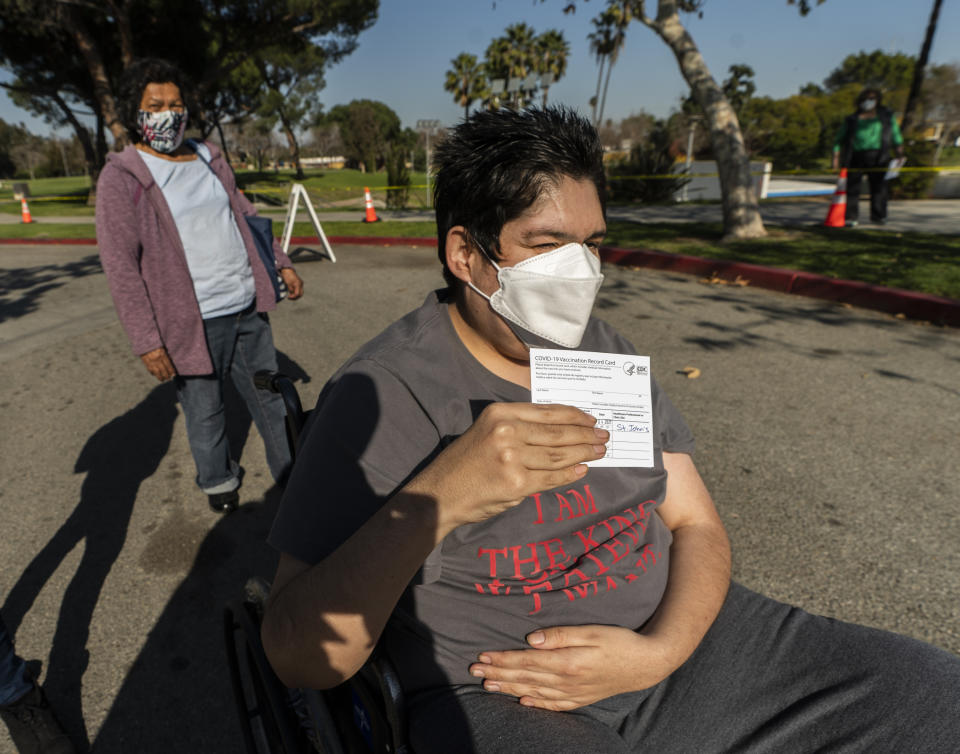 Cancer survivor, Joel Flores, who has Autism Spectrum Disorder, holds up his vaccination card after being able to receive his first vaccine shot at the COVID-19 vaccination site at the East Los Angeles Civic Center in Los Angeles on Thursday, March 4, 2021. His mother, Emilia del Carmen Flores, left, originally from El Salvador, also got the vaccine. California will begin setting aside 40% of all vaccine doses for the state's most vulnerable neighborhoods in an effort to inoculate people most at risk from the coronavirus more quickly. (AP Photo/Damian Dovarganes)