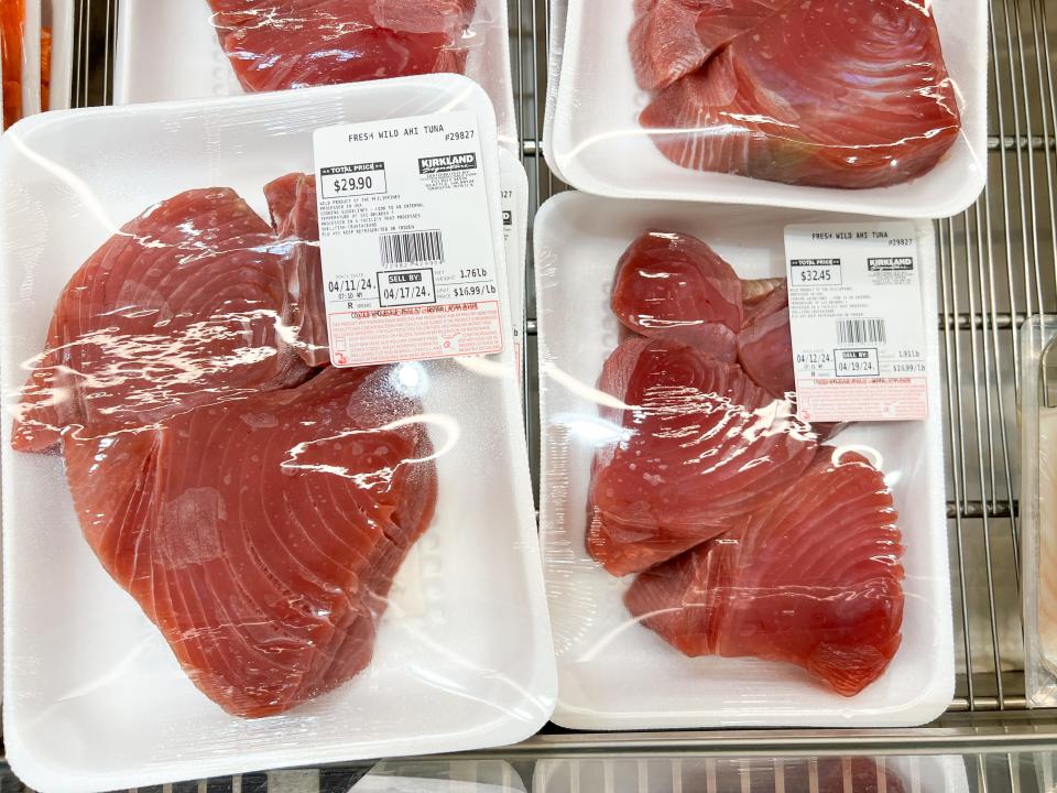 White plastic trays with slabs on ahi tuna with white labels with prices and Kirkland Signature label