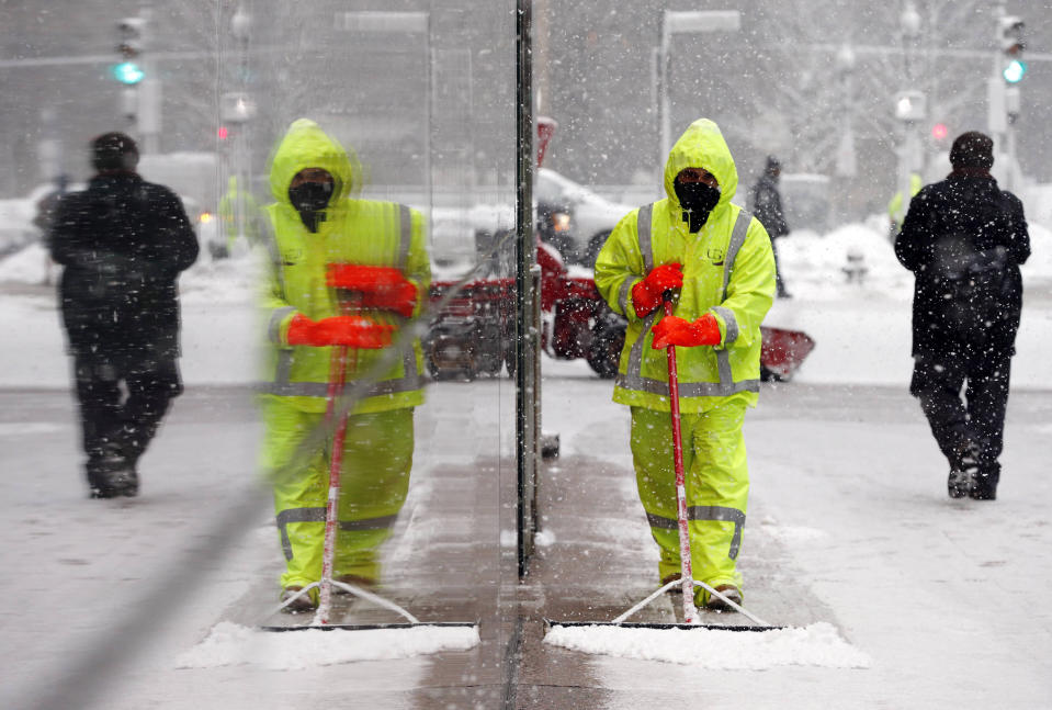 A worker is reflected in a building facade as he clears snow from the sidewalk in Boston, Tuesday, Feb. 18, 2014. It was expected to drop 3 to 5 inches of snow on Boston, with 6 to 10 inches forecast for parts of Northern New England, before moving out late Tuesday and early Wednesday. (AP Photo/Michael Dwyer)