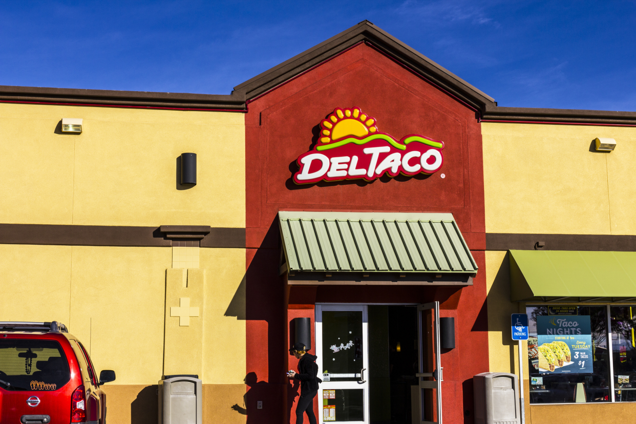 Front exterior of Del Taco fast food restaurant, St. George, Utah, front doors and windows with a person walking out, a car is parked, against a blue sky