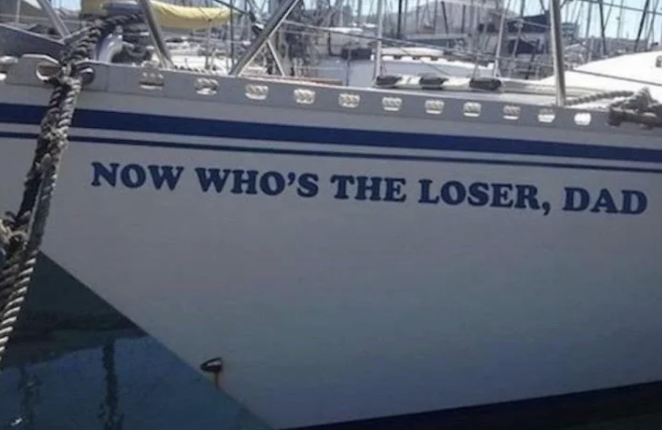 The side of a boat docked in a marina displays the humorous text: "NOW WHO'S THE LOSER, DAD."