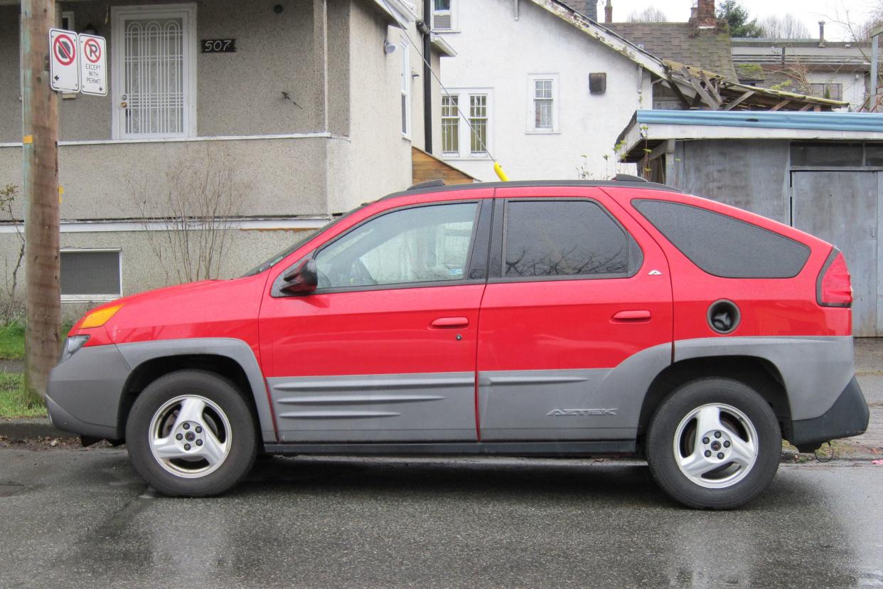 Red Pontiac Aztek parked on rainy street.