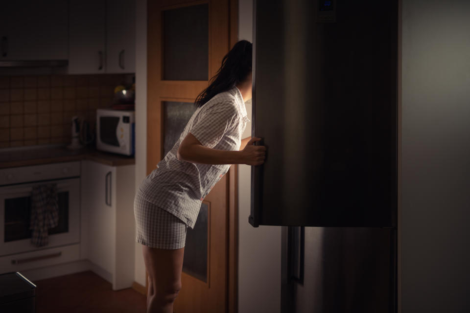 Woman opening her fridge at night searching for food 