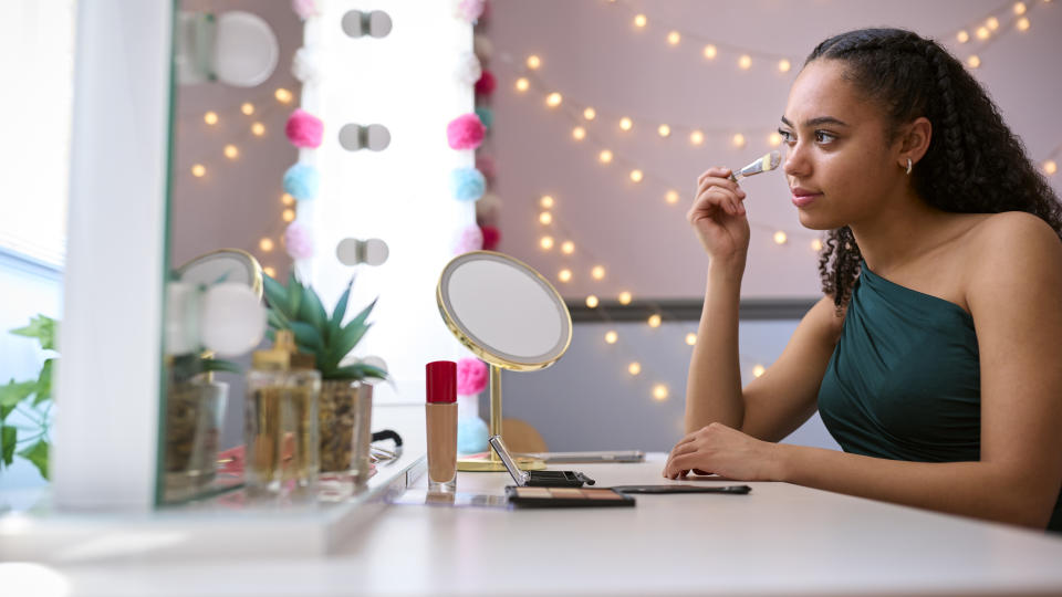 a teen putting on makeup in their bedroom