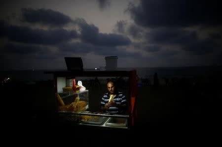 A Palestinian vendor sells snacks on a beach during a power cut as he uses battery-powered lights in Gaza City, July 12, 2017. REUTERS/Mohammed Salem/Files