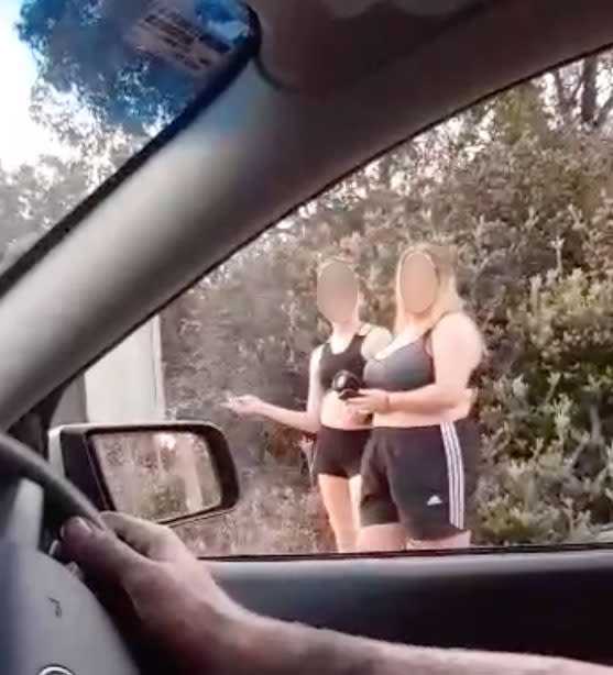Two girls girls shown after lighting their clothes on fire on a road alongside dense bushland in Perth.