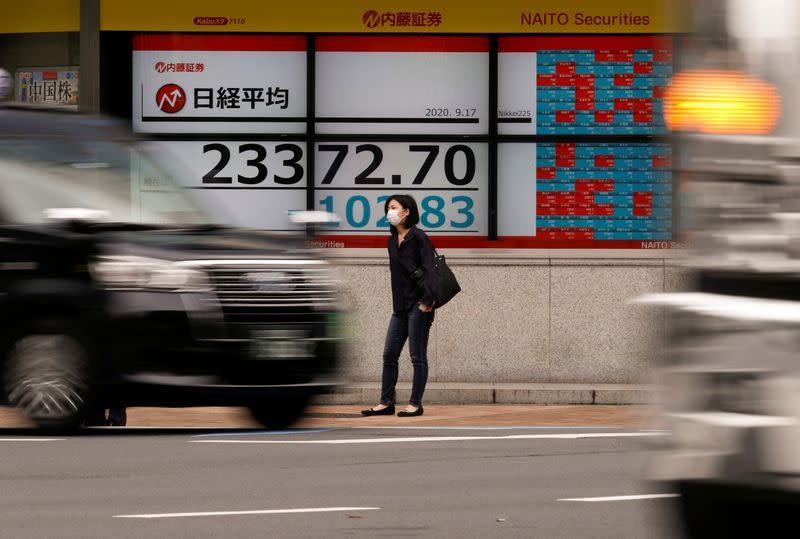 A passerby wearing a protective face mask stands in front of an electronic board showing Japan's Nikkei averageoutside a brokerage, amid the coronavirus disease (COVID-19) outbreak, in Tokyo