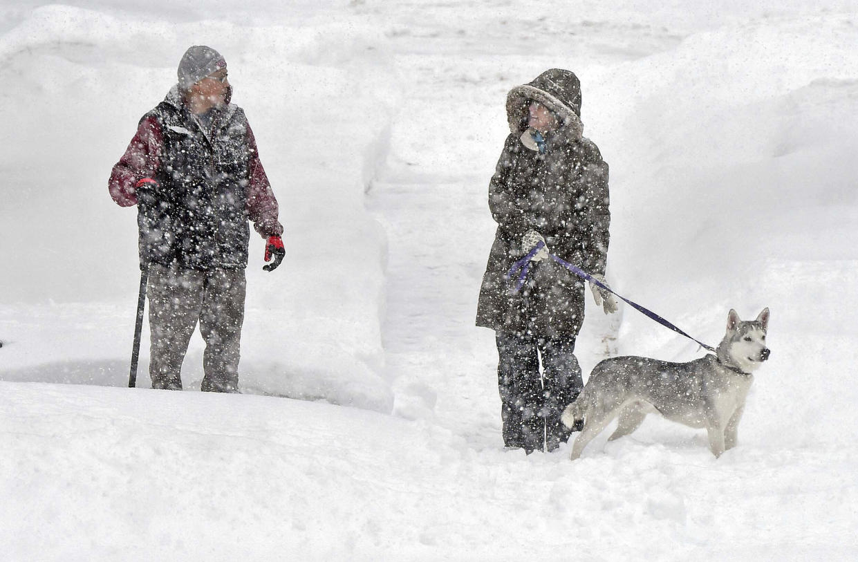 Gordon Weyaus, left, and Katy Little with dog Jax walk along Mandan Street in Bismarck, N.D., in the snow on Wednesday, Dec. 14, 2022. (Tom Stromme/The Bismarck Tribune via AP)