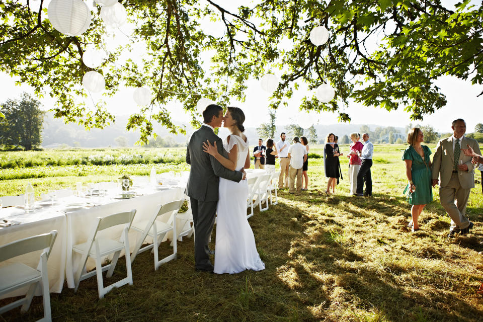wedding  Bride and groom embracing about to kiss near banquet table set for dinner guests in background
