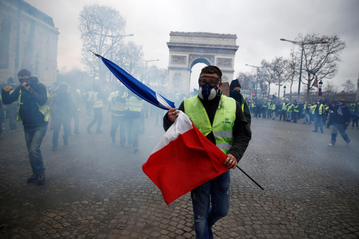 A protester wearing a yellow vest holds a French flag as he walks among tear gas on the Champs-Elysees Avenue near the Arc de Triomphe during a national day of protest by the “yellow vests” movement in Paris, France, Dec. 8, 2018. (Photo: Christian Hartmann/Reuters)