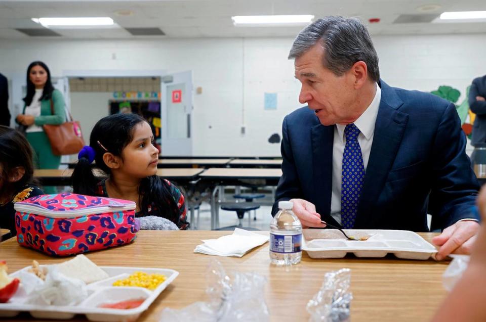 Gov. Roy Cooper speaks with kindergarten student Sankeerthana Lolla while eating lunch at Bethesda Elementary School in Durham, N.C in October 2022. Cooper visited the school to announce new agreements to bring food from North Carolina farmers and producers to schools.