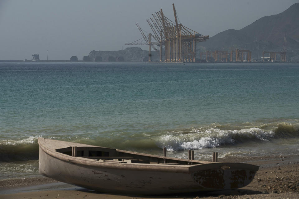 A wooden boat sits on the beach with the Port of Khorfakkan behind it in Khorfakkan, United Arab Emirates, Saturday, June 15, 2019. The Japanese owner of the Kokuka Courageous said Friday, June 14, 2019, that the vessel, one of two oil tankers targeted in an apparent attack in the Gulf of Oman, would be brought to the Emirati port of Khorfakkan. (AP Photo/Jon Gambrell)