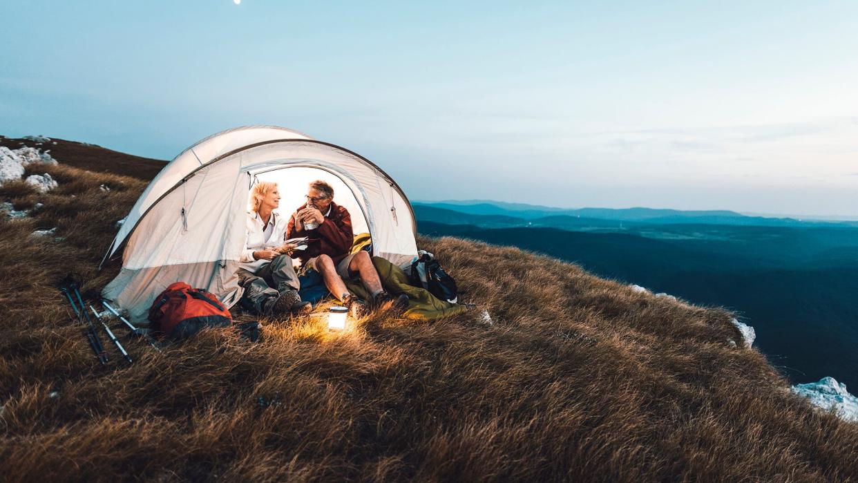 Senior couple camping in the mountains and eating a snack.